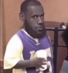 a man in a purple jersey is holding a remote control and making a funny face .