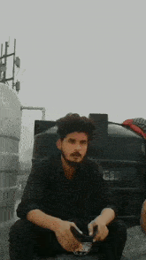 a man with a beard is sitting in front of a black water tank .