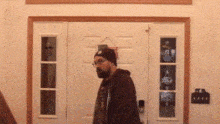 a man with a beard and glasses is standing in front of a white door .