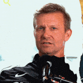a man is speaking into a microphone with a nike logo on his shirt