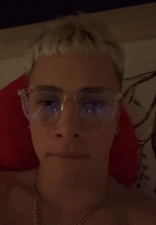 a man wearing glasses and a necklace is laying on a bed