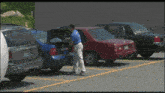 a man in a blue shirt is putting something in the trunk of a blue car