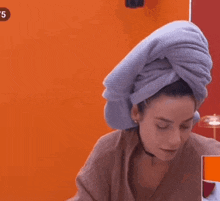 a woman with a towel wrapped around her head is sitting in front of an orange wall .