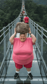 a man in a pink shirt holds a large rock over his head