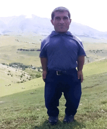 a man in a blue shirt is standing on a grassy hillside