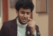 a man in a suit and turtleneck is making a funny face while pointing at his nose .