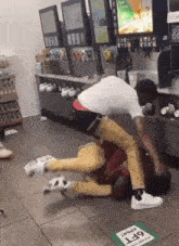 two men are fighting in a gas station and one of them is laying on the floor .