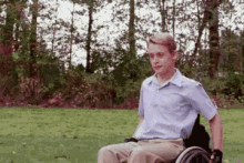 a young man is sitting in a wheelchair in a park with trees in the background