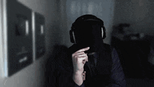 a man wearing headphones and a hat is covering his face with his hand .