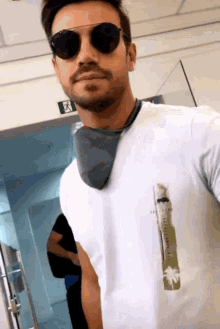 a man wearing sunglasses and a white t-shirt with a palm tree on the front takes a selfie