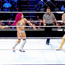 a woman with pink hair is standing in a wrestling ring with a referee .