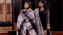 two women are standing next to each other covered in a blanket .