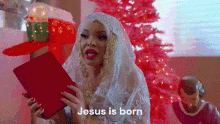 a woman is singing a christmas song in front of a pink christmas tree while holding a book .
