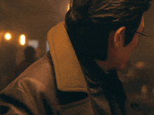 a man wearing glasses and a trench coat looks at the camera