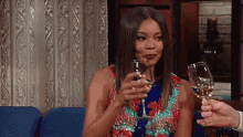 a woman is sitting on a couch holding a glass of wine and toasting .