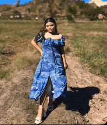 a woman wearing a blue dress and white heels stands in a field