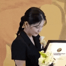 a woman in a black dress is holding a framed certificate .