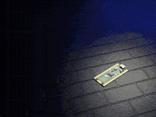a green and gold motherboard is laying on a black brick floor