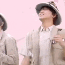 a man wearing a hat and a vest is standing next to another man .