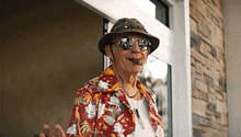 a man wearing a hat and sunglasses is standing in front of a doorway