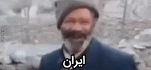 a man with a beard and mustache is wearing a hat and a jacket and talking in a foreign language .
