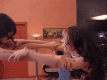 two women are fighting in front of a painting of fruit on the wall