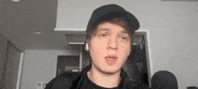 a young man wearing a black hat and ear buds is talking into a microphone .