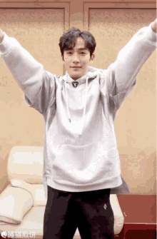 a man in a white hoodie is standing with his arms outstretched in front of a couch