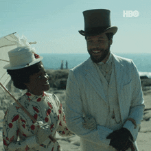 a man in a top hat stands next to a woman holding an umbrella with the hbo logo in the background