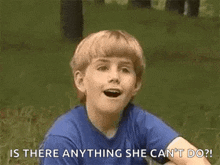 a young boy in a blue shirt is sitting in the grass looking up .