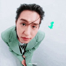 a man in a green suit is looking at the camera with a green dinosaur behind him that says bbbillkin gif
