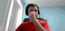 a man wearing headphones and a red shirt is sitting in a chair covering his nose .
