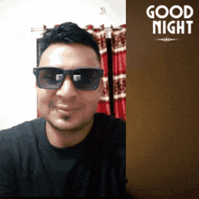 a man wearing sunglasses is smiling in front of a sign that says " good night "