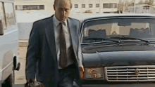 a man in a suit and tie is walking towards a black car .