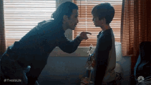 a man is pointing at a young boy in front of a window with blinds on it ..