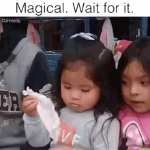 two little girls are sitting next to each other and one is holding a piece of paper that says " magical wait for it "