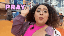 a woman in a pink shirt and purple jacket with the word pray above her head