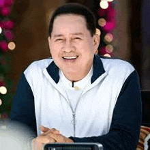 a man in a white and blue jacket is smiling while sitting at a table .