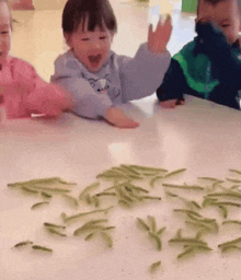 a group of children are sitting at a table with green beans on it