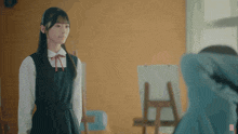 a girl in a school uniform stands next to another girl in a blue coat
