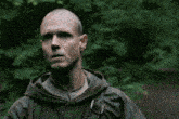 a bald man in a hooded jacket is pointing at the camera