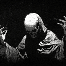 a black and white photo of a skeleton in a robe with his hands outstretched in the dark .