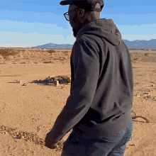 a man wearing a black hoodie and a hat stands in the desert