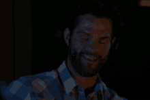 a man with a beard wearing a plaid shirt is smiling in the dark