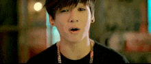 a young man wearing a black shirt and a necklace is looking at the camera with his mouth open .