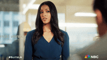 a woman in a blue dress is standing next to a man in a nbc advertisement