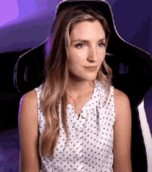 a woman in a white shirt is sitting in a chair and looking at the camera .