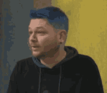 a man with blue hair is wearing a black hoodie and looking at the camera .
