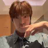 a young man wearing a denim shirt is making a funny face with his hand on his chin .