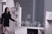 a woman in a black dress is standing in front of a table with wine glasses on it